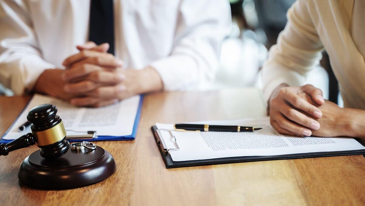 Two people sit at a table with official documents, a hammer and gavel, and two rings.