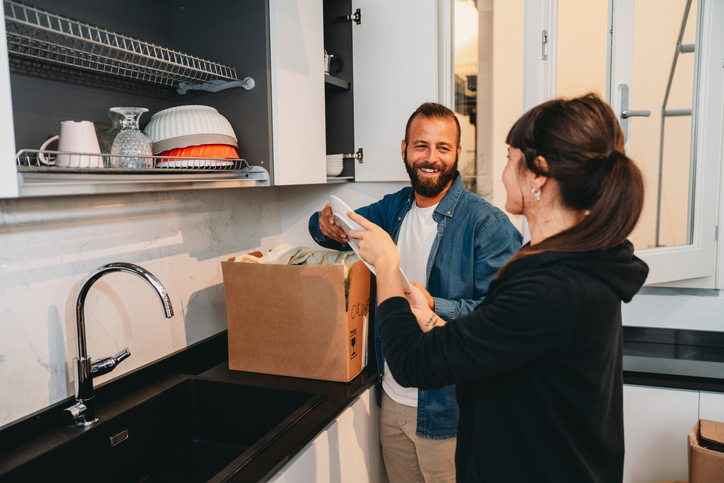 A man and woman are smiling and boxing items in a modern kitchen.