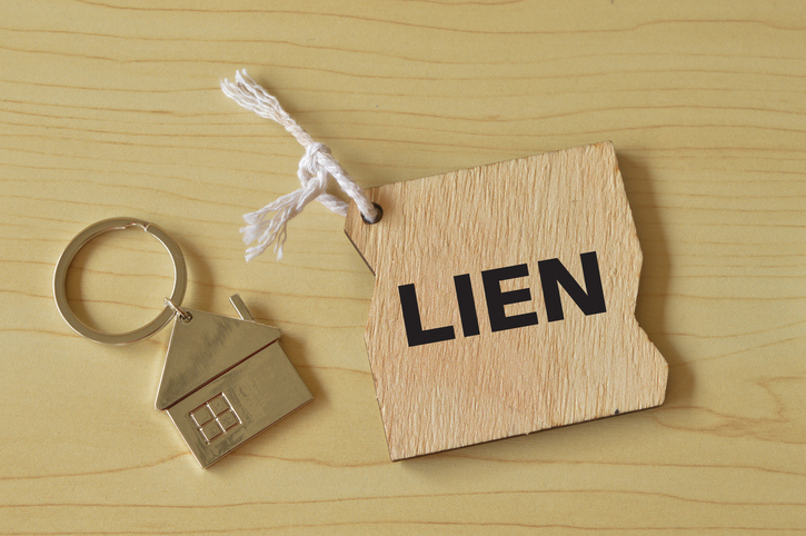 A house-shaped keyring next to a tag with the word "LIEN" on it, placed on a wooden surface.