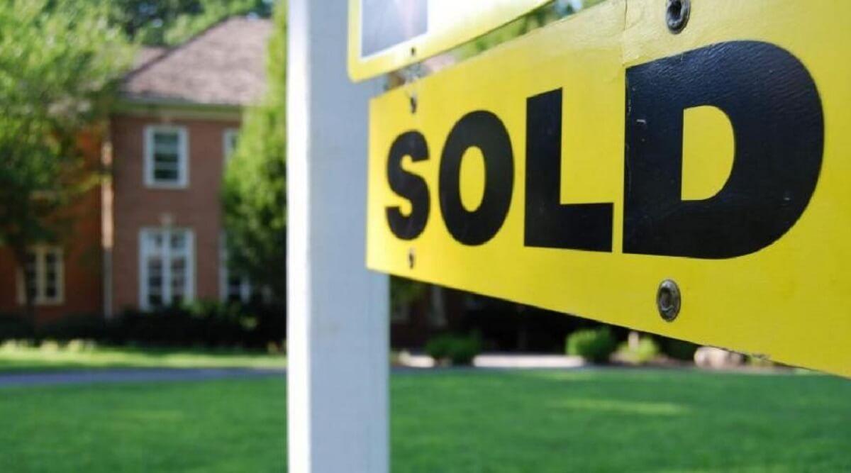 Closeup of a yellow and black sold sign in front of a house.