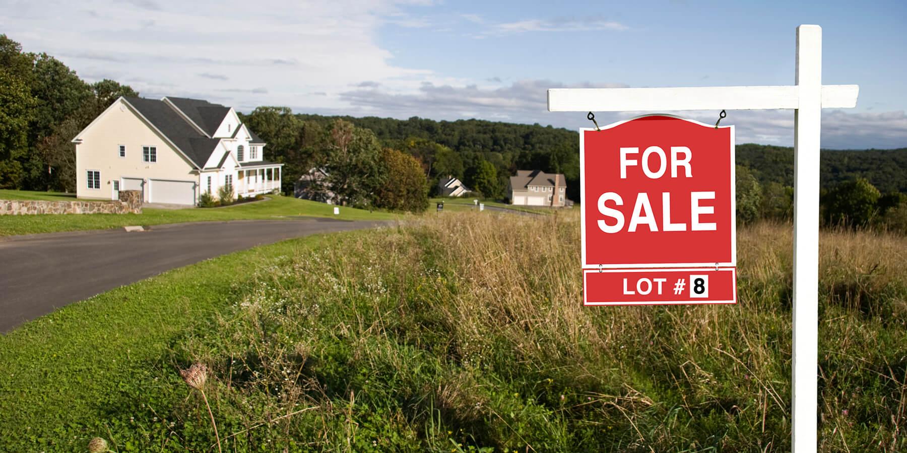 Red and white for sale sign in front of a large plot of land.