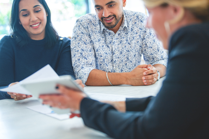 A cheerful couple attentively listens to a real estate agent, who is presenting a document during a meeting.